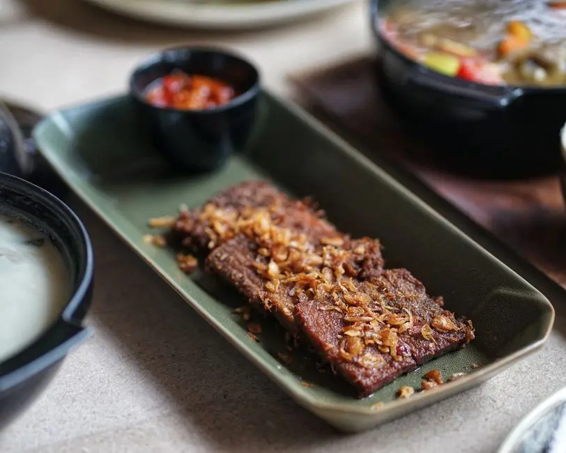 Piring berisi sop iga sapi dengan kuah bening, pelengkap sambal terasi dan lalapan