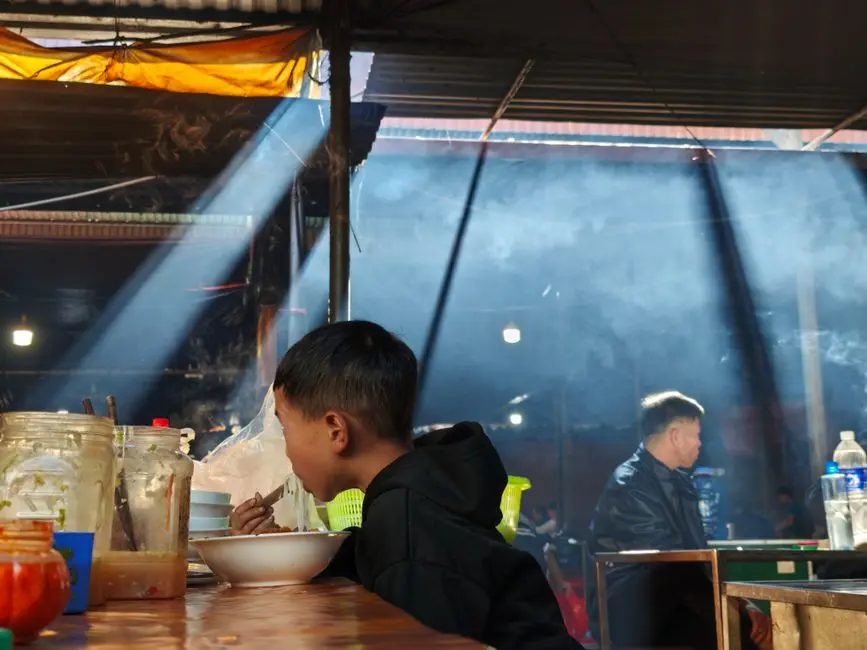 Suasana warung Mbok Inem dengan meja kayu dan bangku plastik di dalam gang